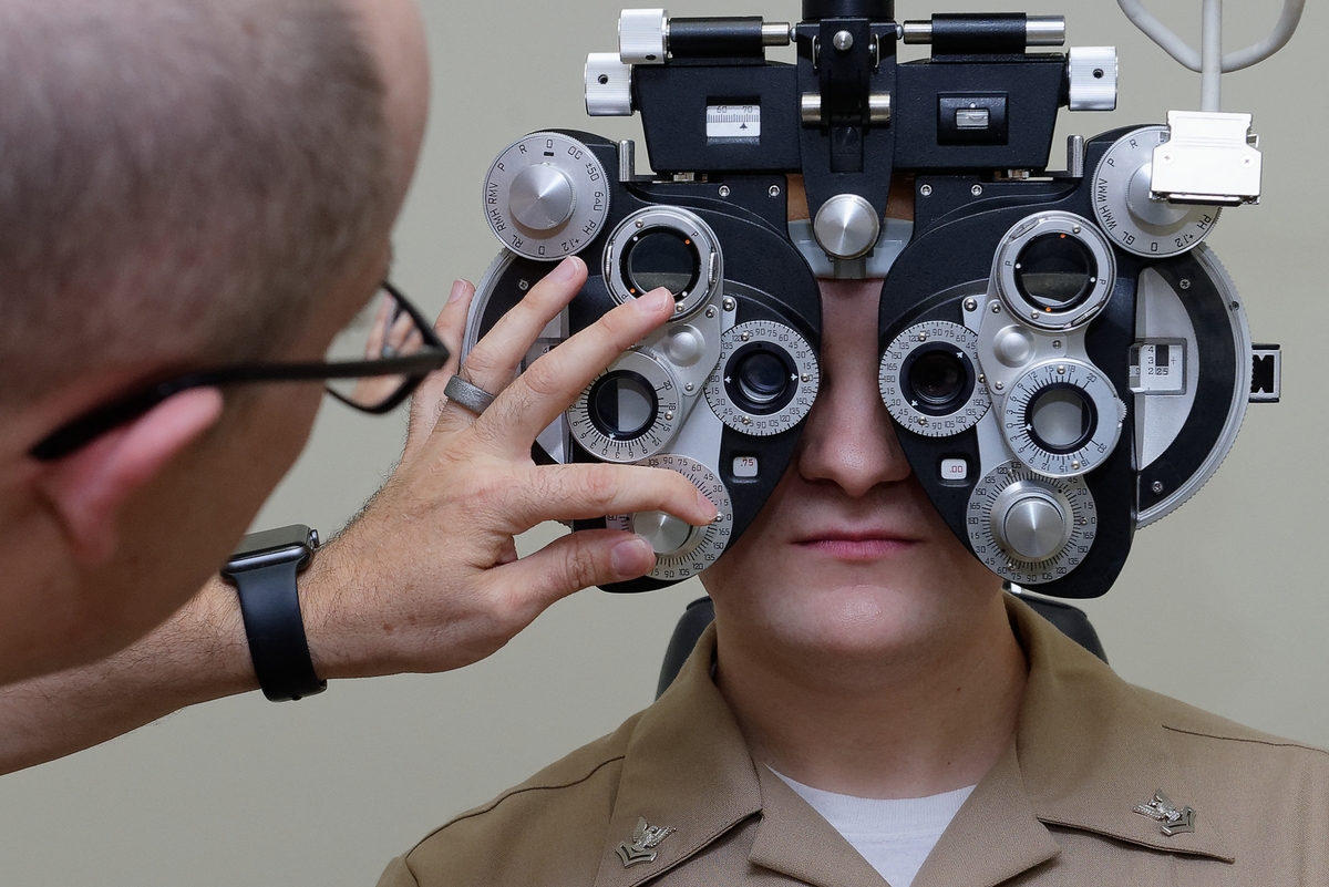 Person undergoing an eye exam, looking into a phoropter